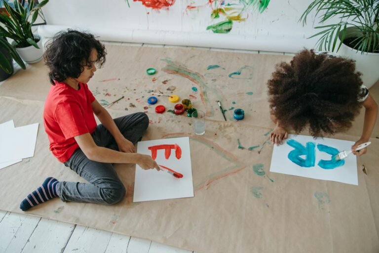 Two children painting with watercolors on paper, exploring creativity and art.